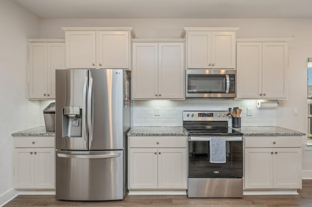 kitchen featuring light stone counters, stainless steel appliances, backsplash, and wood finished floors