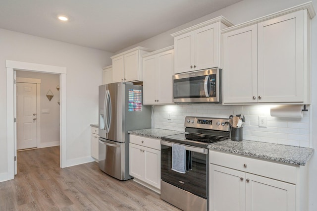 kitchen with stainless steel appliances, light wood-type flooring, light stone counters, and tasteful backsplash