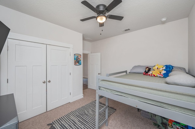 carpeted bedroom featuring a closet, visible vents, ceiling fan, and a textured ceiling