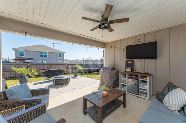 view of patio featuring ceiling fan, an outdoor living space with a fire pit, a trampoline, and fence