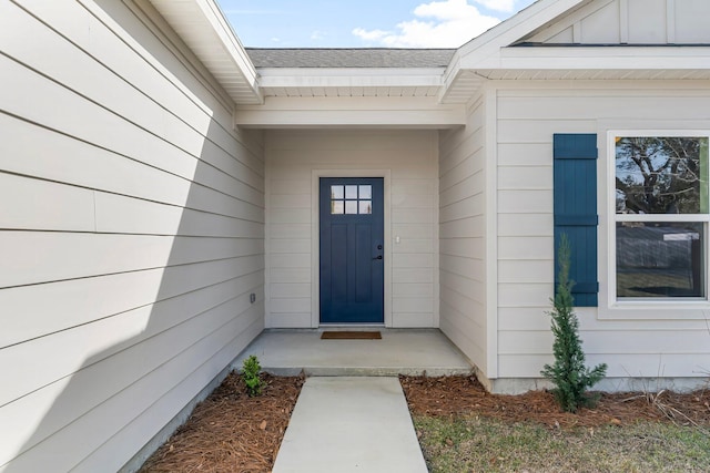 view of exterior entry with a shingled roof and board and batten siding