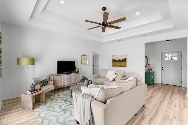 living room with ceiling fan, light wood-type flooring, a raised ceiling, and recessed lighting