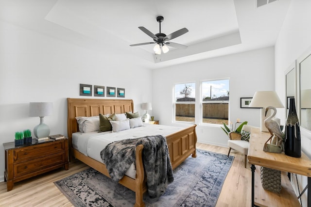 bedroom featuring a tray ceiling, ceiling fan, and light wood finished floors