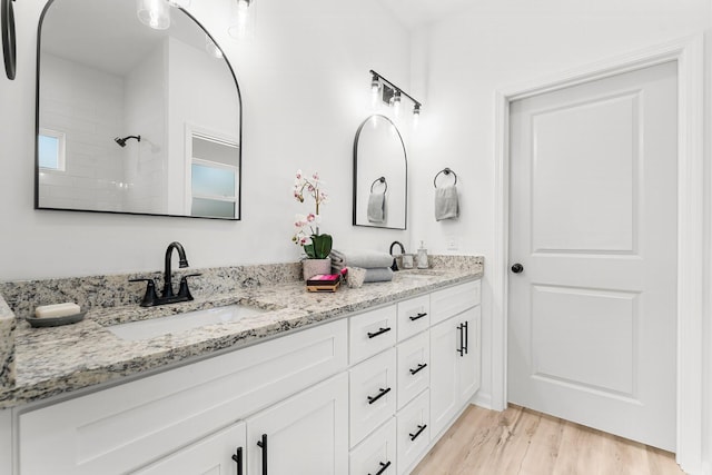 bathroom with double vanity, a shower, a sink, and wood finished floors