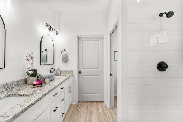 bathroom with double vanity, a sink, wood finished floors, and tiled shower