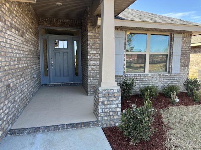 entrance to property with brick siding and a shingled roof