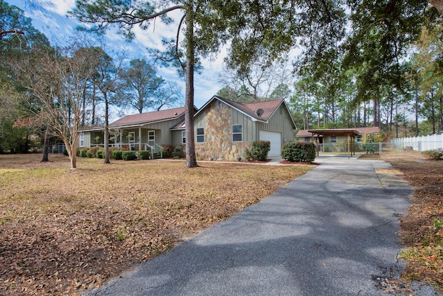 ranch-style house featuring fence, covered porch, stone siding, aphalt driveway, and board and batten siding