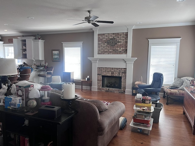 living room with wood finished floors, baseboards, ornamental molding, ceiling fan, and a brick fireplace