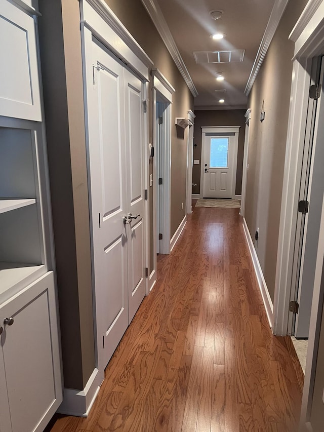 hallway with crown molding, wood finished floors, visible vents, and baseboards