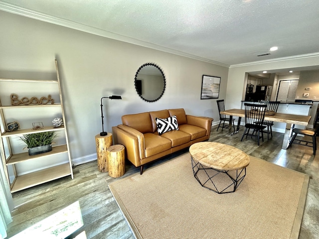 living area featuring a textured ceiling, wood finished floors, visible vents, baseboards, and ornamental molding