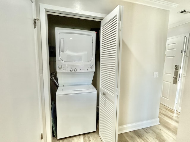 washroom with laundry area, light wood-type flooring, stacked washing maching and dryer, and visible vents