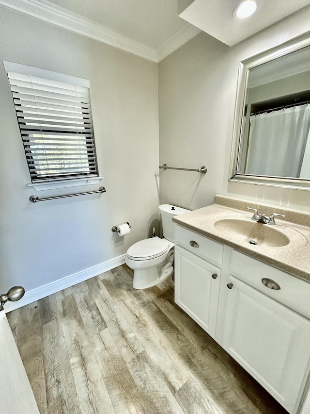 bathroom featuring baseboards, toilet, wood finished floors, crown molding, and vanity