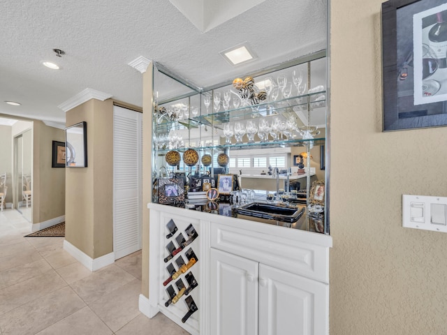 bar featuring light tile patterned floors, a textured ceiling, baseboards, and indoor wet bar