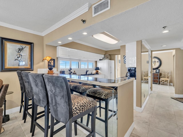 kitchen with a textured ceiling, visible vents, white cabinets, ornamental molding, and freestanding refrigerator