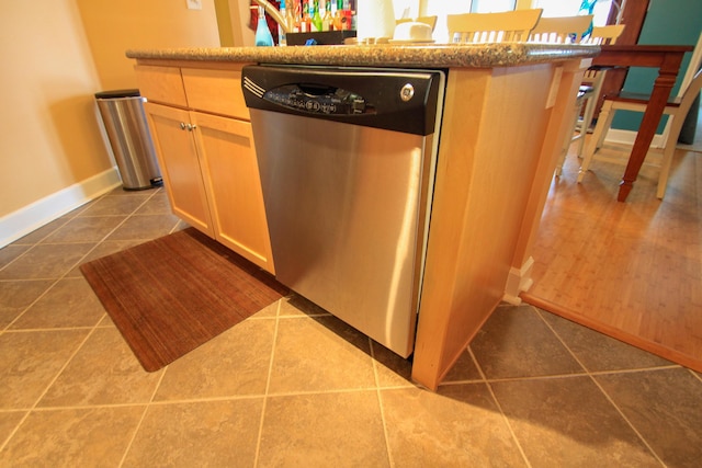 kitchen featuring dark tile patterned floors, baseboards, and stainless steel dishwasher