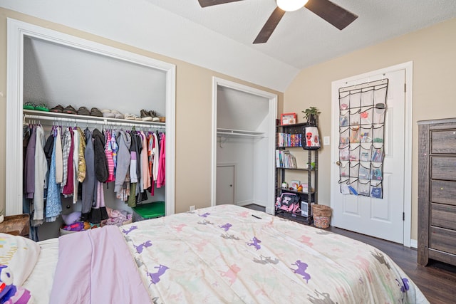 bedroom with lofted ceiling, ceiling fan, wood finished floors, a textured ceiling, and two closets