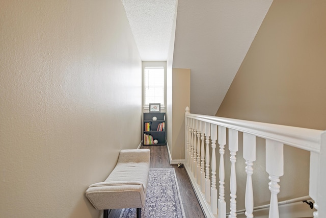 hallway featuring dark wood-type flooring, a textured wall, a textured ceiling, and baseboards