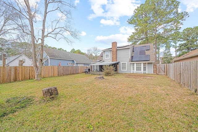 back of property featuring a fenced backyard, a chimney, solar panels, and a yard