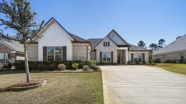 view of front of property featuring board and batten siding, roof with shingles, a front lawn, central AC, and brick siding