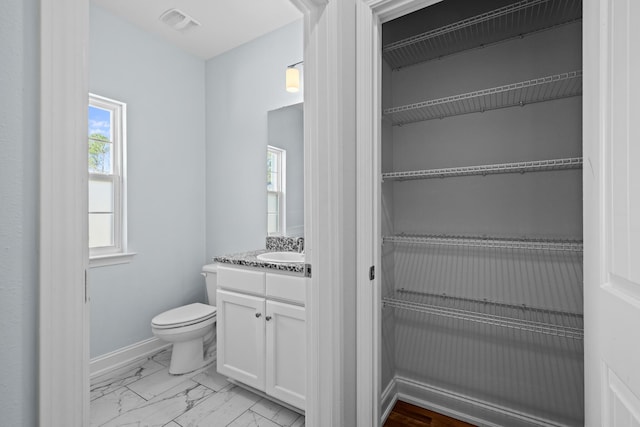 bathroom featuring toilet, visible vents, vanity, baseboards, and marble finish floor