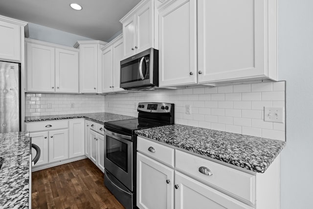 kitchen featuring dark stone counters, appliances with stainless steel finishes, dark wood-style flooring, and white cabinetry