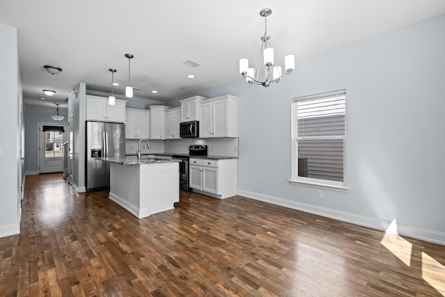 kitchen with tasteful backsplash, dark wood-style floors, appliances with stainless steel finishes, dark stone countertops, and a kitchen island with sink