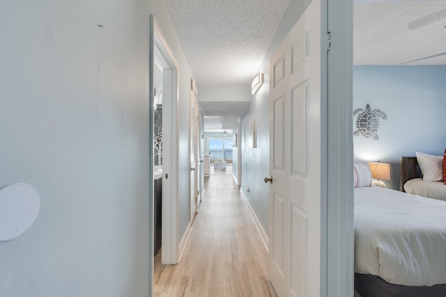 corridor with light wood-style floors, a textured ceiling, and baseboards