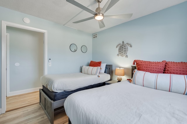 bedroom with a textured ceiling, baseboards, light wood-style flooring, and a ceiling fan