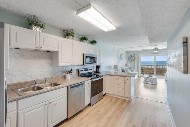 kitchen with appliances with stainless steel finishes, a peninsula, a sink, light wood-type flooring, and backsplash