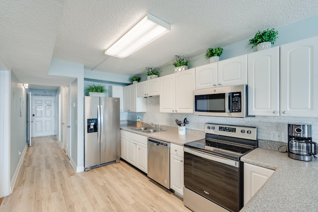 kitchen featuring tasteful backsplash, stainless steel appliances, light wood-type flooring, white cabinetry, and a sink