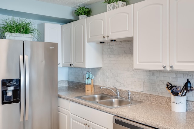 kitchen featuring stainless steel appliances, backsplash, a sink, and white cabinets