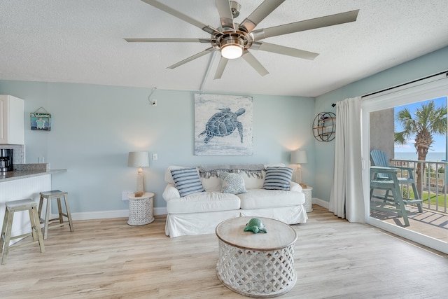 living area with light wood finished floors, baseboards, a ceiling fan, and a textured ceiling