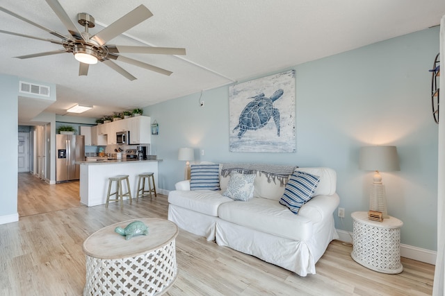 living area featuring ceiling fan, light wood-type flooring, visible vents, and baseboards