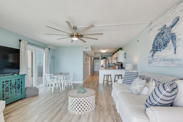 living area featuring light wood-style flooring, visible vents, ceiling fan, and a textured ceiling