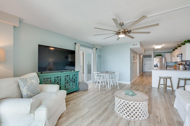 living area featuring visible vents, ceiling fan, a textured ceiling, and light wood finished floors