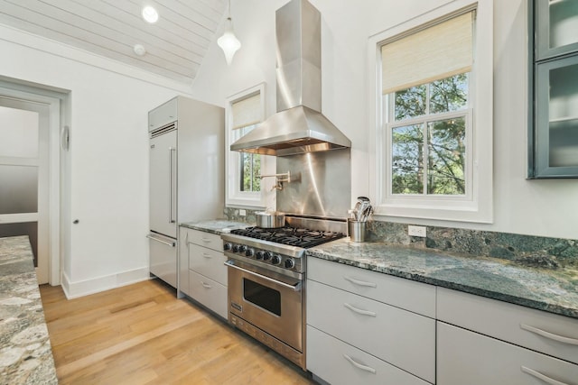 kitchen with dark stone countertops, premium stove, ventilation hood, and vaulted ceiling