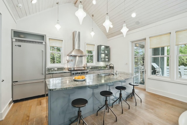 kitchen featuring light wood finished floors, a sink, built in fridge, wall chimney range hood, and range