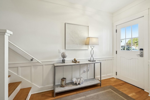 foyer entrance with stairway, a decorative wall, a wainscoted wall, and wood finished floors