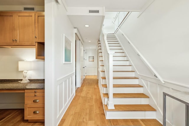 staircase featuring visible vents, built in study area, a decorative wall, and wood finished floors