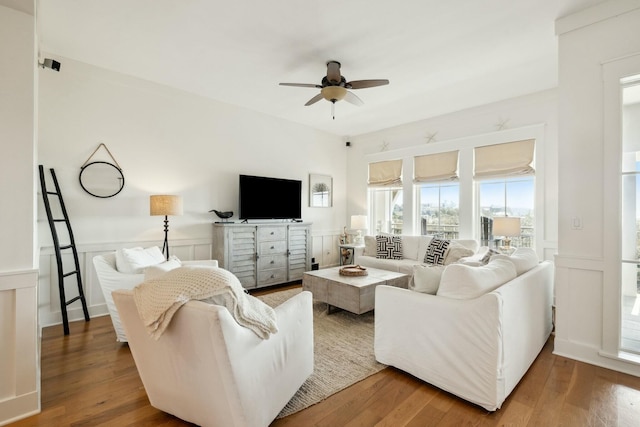 living room featuring a decorative wall, wainscoting, ceiling fan, and wood finished floors