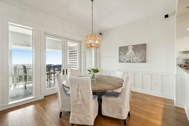 dining space featuring a notable chandelier, a decorative wall, wainscoting, and wood finished floors