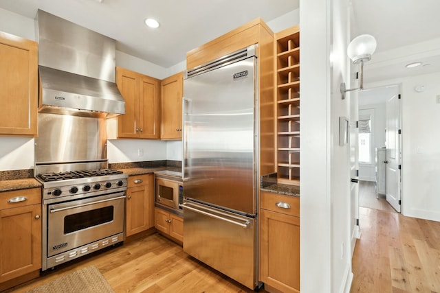 kitchen with extractor fan, light wood-type flooring, built in appliances, and dark stone counters