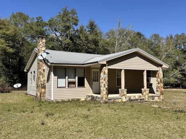 view of front of property featuring covered porch, a chimney, metal roof, and a front yard