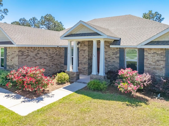 view of front of property with brick siding, a front lawn, and a shingled roof