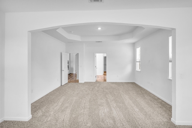 interior space with arched walkways, carpet flooring, a raised ceiling, and baseboards