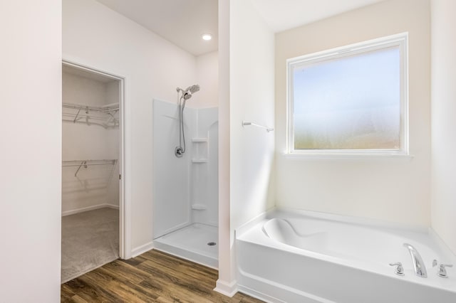 bathroom featuring a walk in shower, a spacious closet, wood finished floors, and a bath