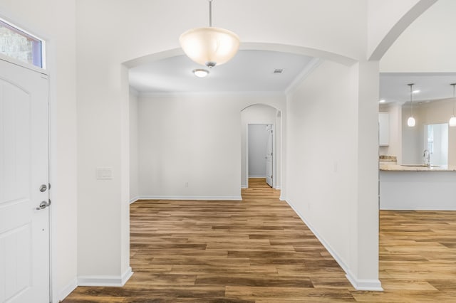 foyer with arched walkways, ornamental molding, and wood finished floors