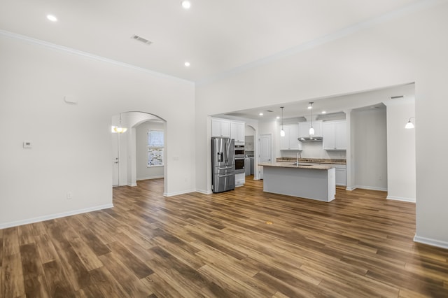 unfurnished living room featuring arched walkways, a sink, baseboards, ornamental molding, and dark wood-style floors