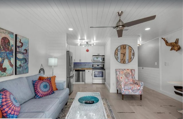 living room featuring wooden ceiling, a wainscoted wall, ceiling fan, and light wood-style flooring