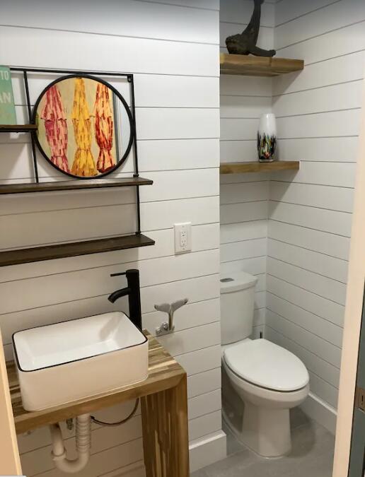 half bathroom with toilet, wood walls, and a sink